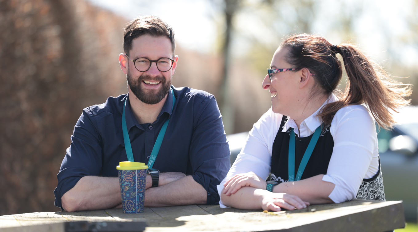 Two CSO employees sit at a table outdoors, smiling and laughing