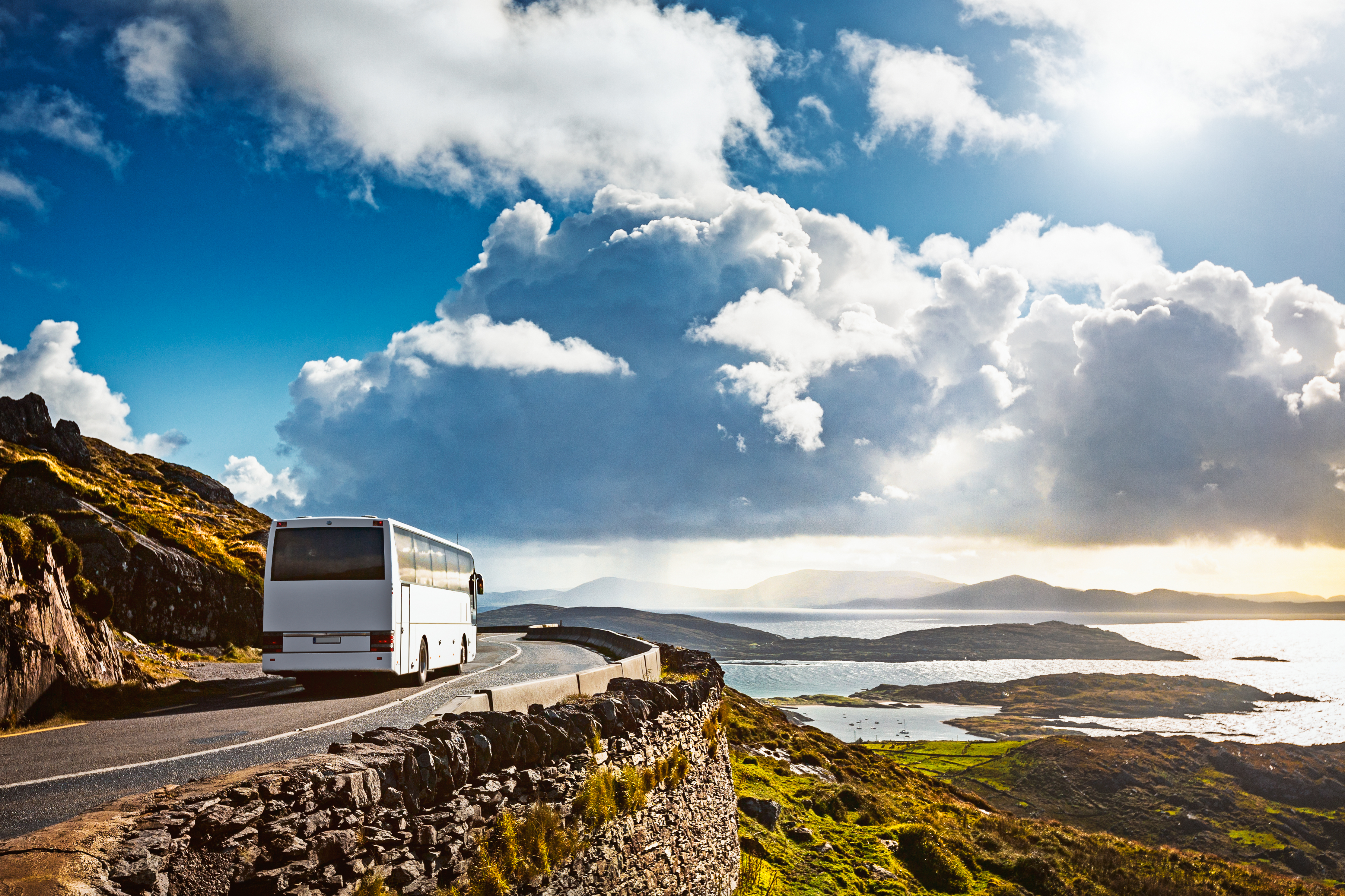 A bus driving along a winding cliff road overlooking a bay with islands